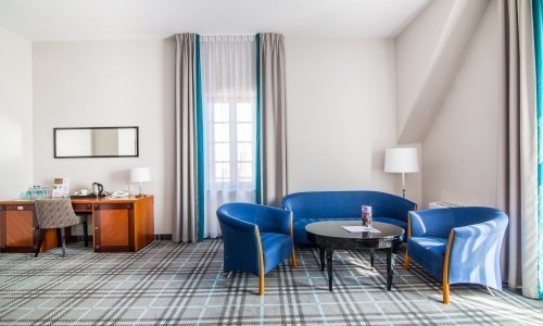Wyposażenie pokoju hotelowego: modne biurko z lustrem, jasne lampy i wygodny wypoczynek ze stolikiem
