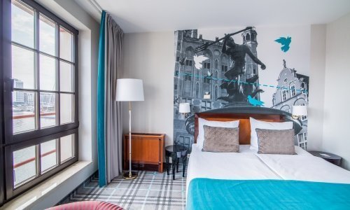 Jasny pokój z dużym łóżkiem udekorowany dodatkami w gdańskich motywach to kwintesencja hotelowego stylu 
