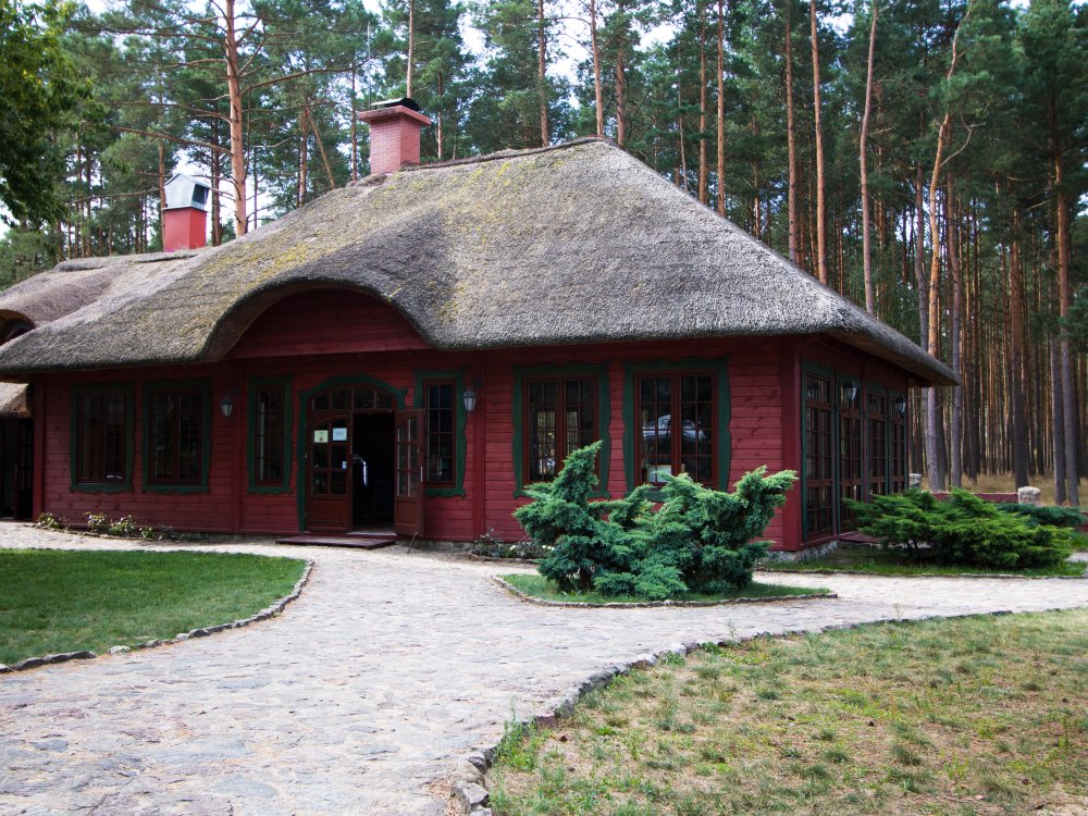 Karczma Largo - drewniany budynek ze strzechą w sosnowym lesie