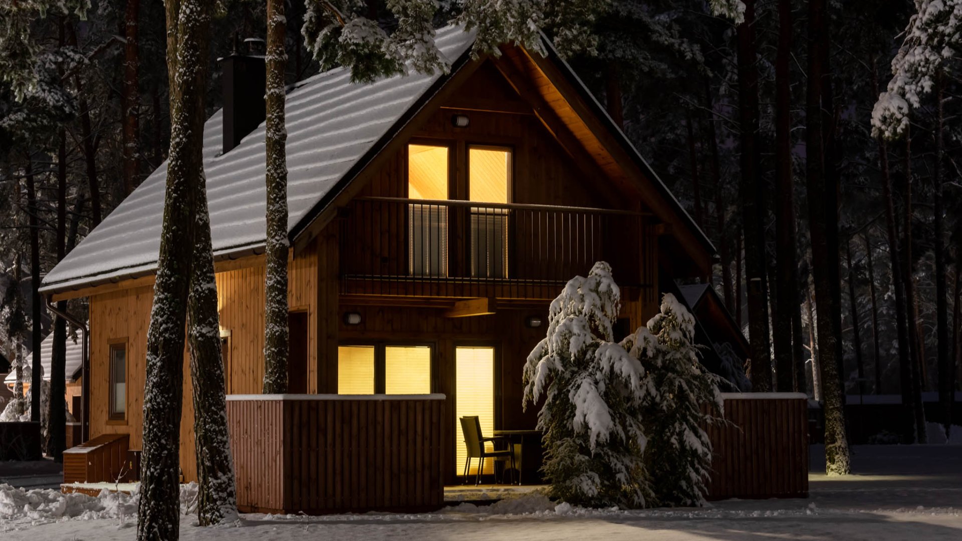 Drewniany domek Largo zimą, nocą, z rozświetlonymi oknami wśród ośnieżonych sosen