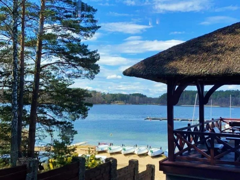 Zadaszona altana nad plażą i turkusową wodą jeziora Wdzydze