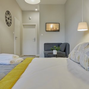 Przytulne łóżko w apartamencie podwójnym w Krakowie, z białą pościelą i dekoracyjnymi poduszkami, w minimalistycznym wnętrzu.