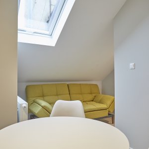 Żółta sofa przy oknie dachowym, tworząca przytulny kącik w apartamencie