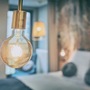 Stylowy detal wnętrza – żarówka wisząca na tle przytulnego pokoju.