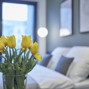 Dekoracyjne kwiaty na stole z widokiem na łóżko w niebiesko-białej sypialni.