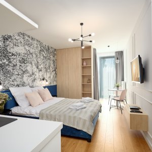 Przestronna przestrzeń z pięknymi niebieskimi akcentami, drewnianymi detalami i elegancką tapetą, zapewniająca przytulny i komfortowy nocleg dla pary w centrum Krakowa