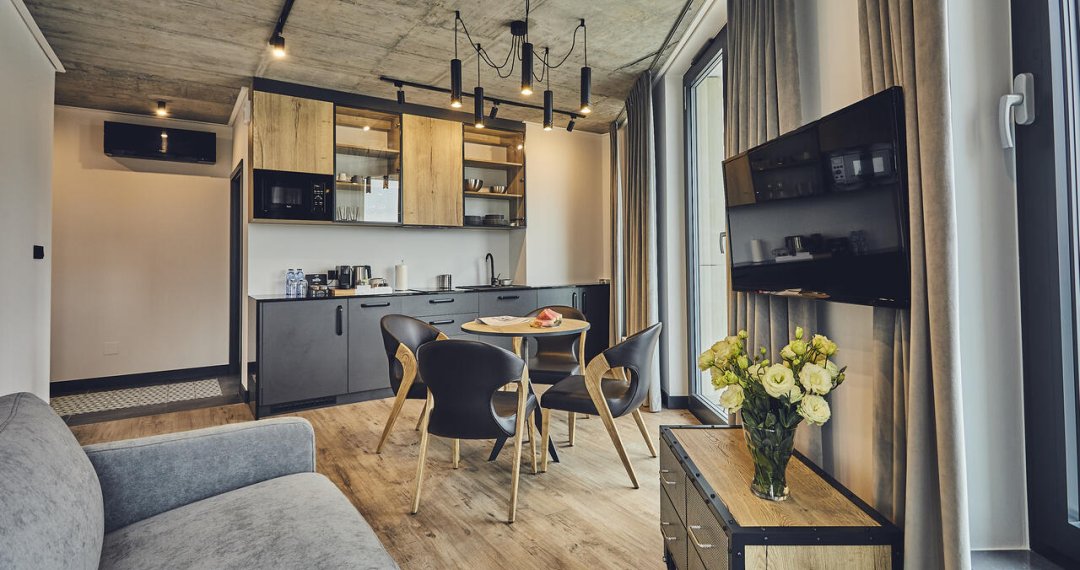 Apartament z nowocześnie wykończonym aneksem kuchennym, wygodną sofą i telewizorem – idealny na dłuższy pobyt w 4-gwiazdkowym hotelu w Krakowie.
