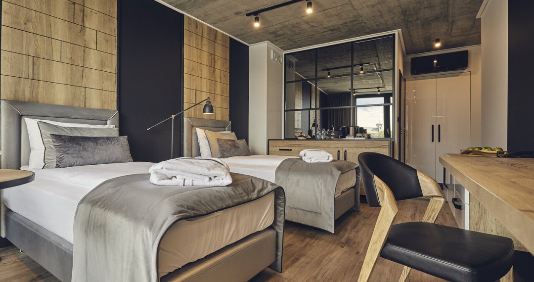 Przestronny pokój hotelowy z dwoma łóżkami, ciepłym drewnianym wystrojem i designerskimi dodatkami