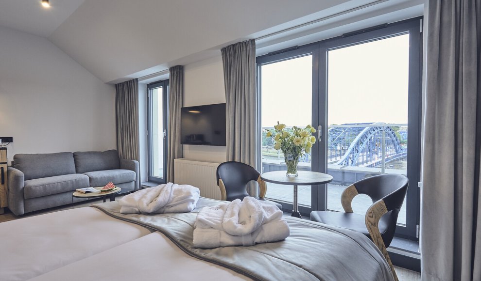 Pokój hotelowy z panoramicznym widokiem na krakowskie Podgórze — komfortowe wnętrze z dużymi oknami i nowoczesnym wystrojem, idealne na wypoczynek w sercu miasta.
